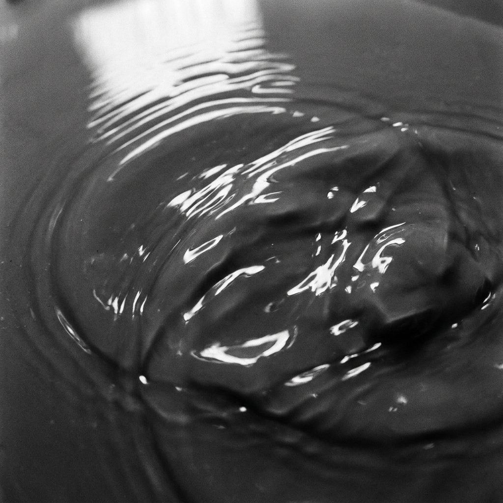 Abstract ripples in dark gray viscous serum liquid, light reflecting off surface